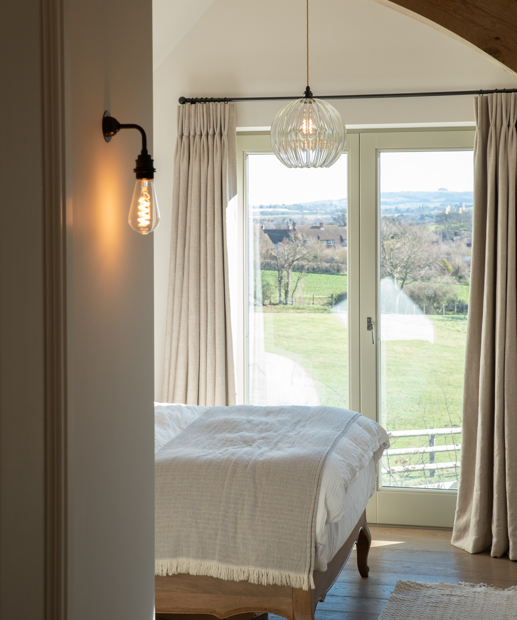 bedroom with small wall light with exposed bulb, glass pendant light and french doors showing view outside