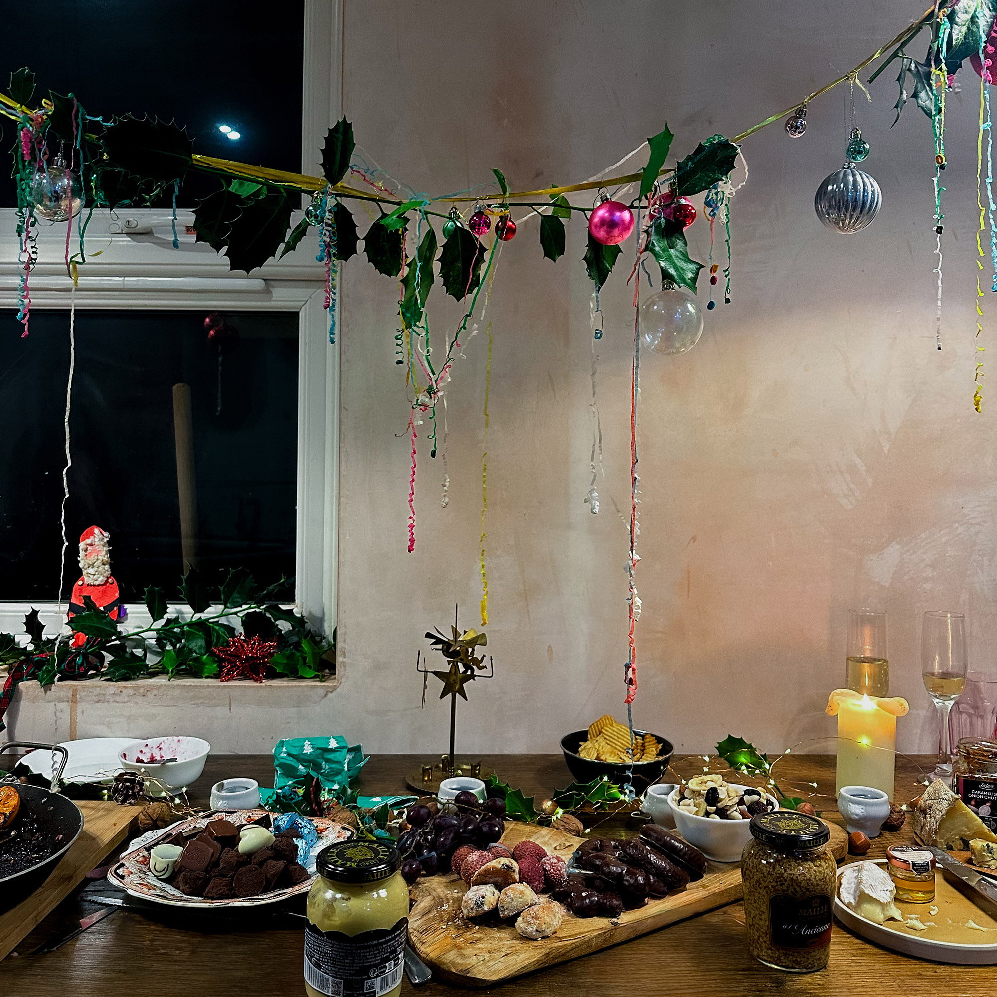 christmas table full of food next to a bare plaster wall with a holly garland hanging above it