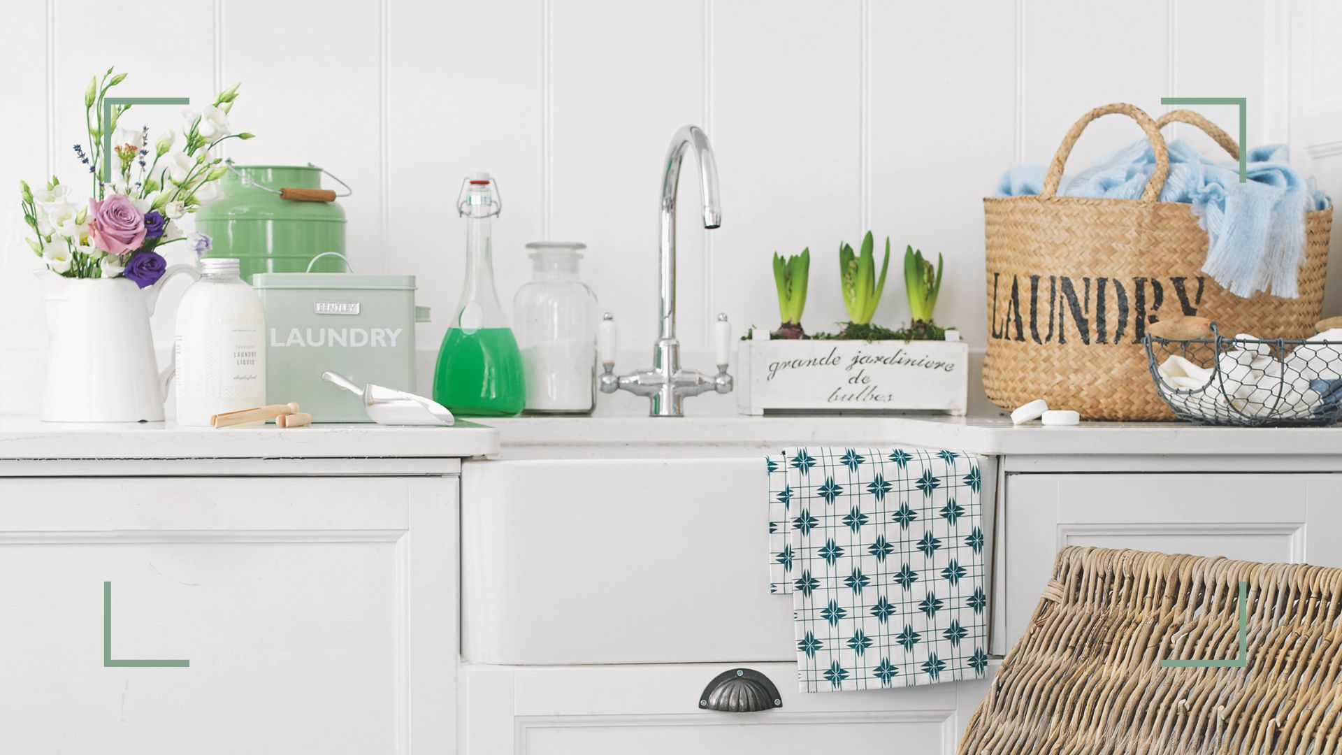 White kitchen with butler sink with countertop filled with laundry baskets and products and spring bulbs and flowers