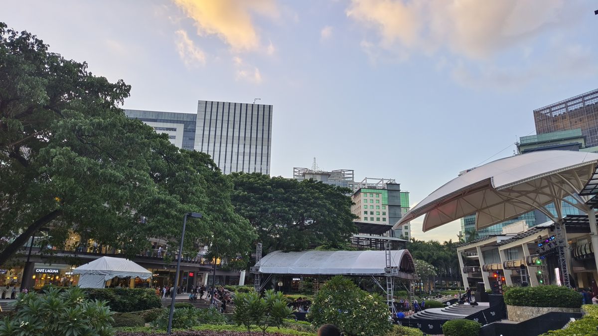A city park with a towering building in the background, surrounded by lush greenery and people enjoying the outdoors