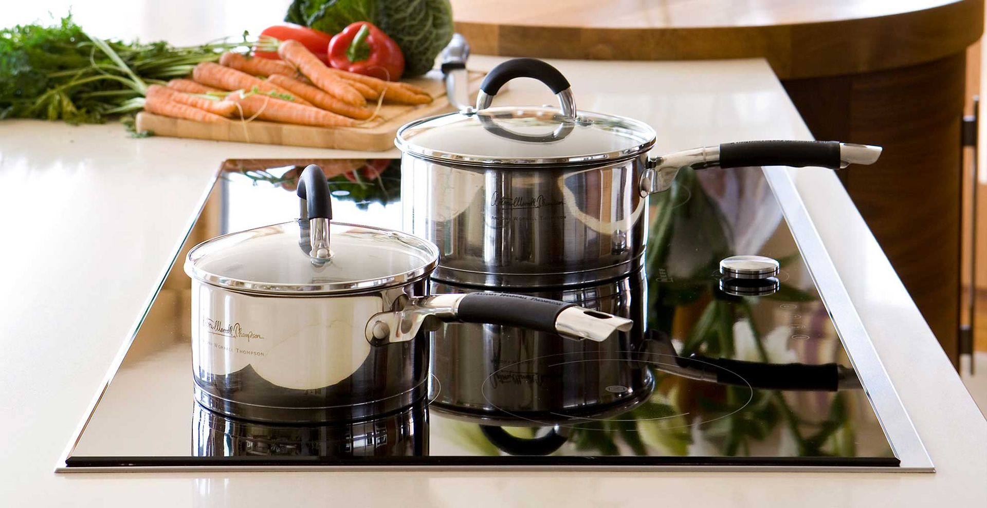 close up of a kitchen countertop with an induction hob with stainless steel pans cooking