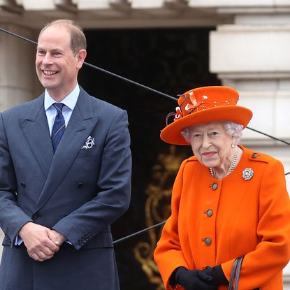 Prince Edward smiles while posing with his mom, Queen Elizabeth II, who wears a bright orange suit