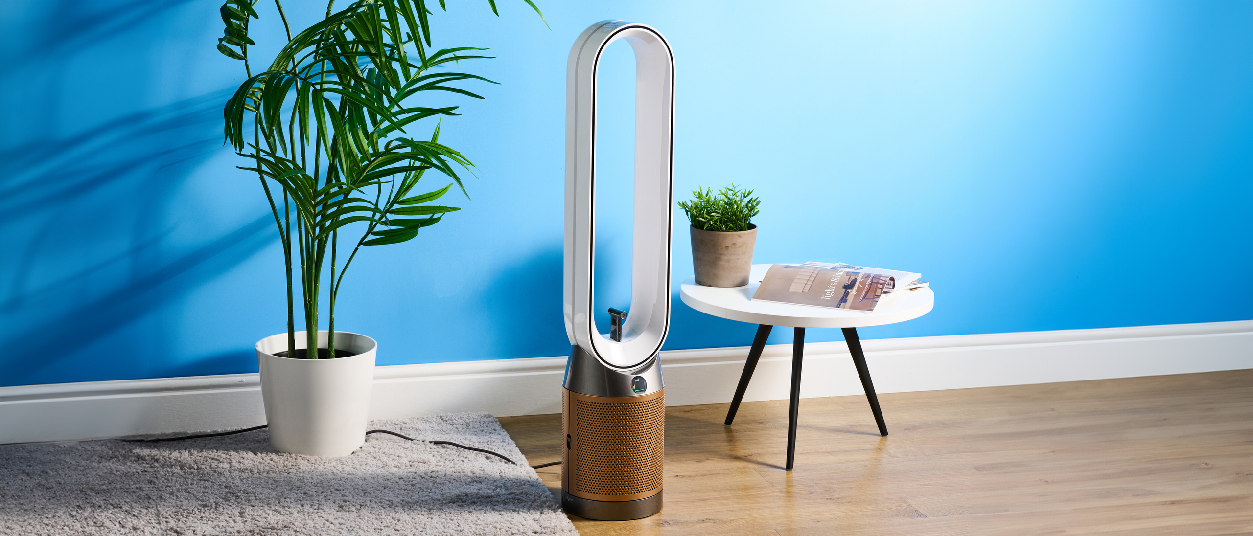 The Dyson Find+Follow Purifier Cool PC3 in a lounge with a blue wall in the background