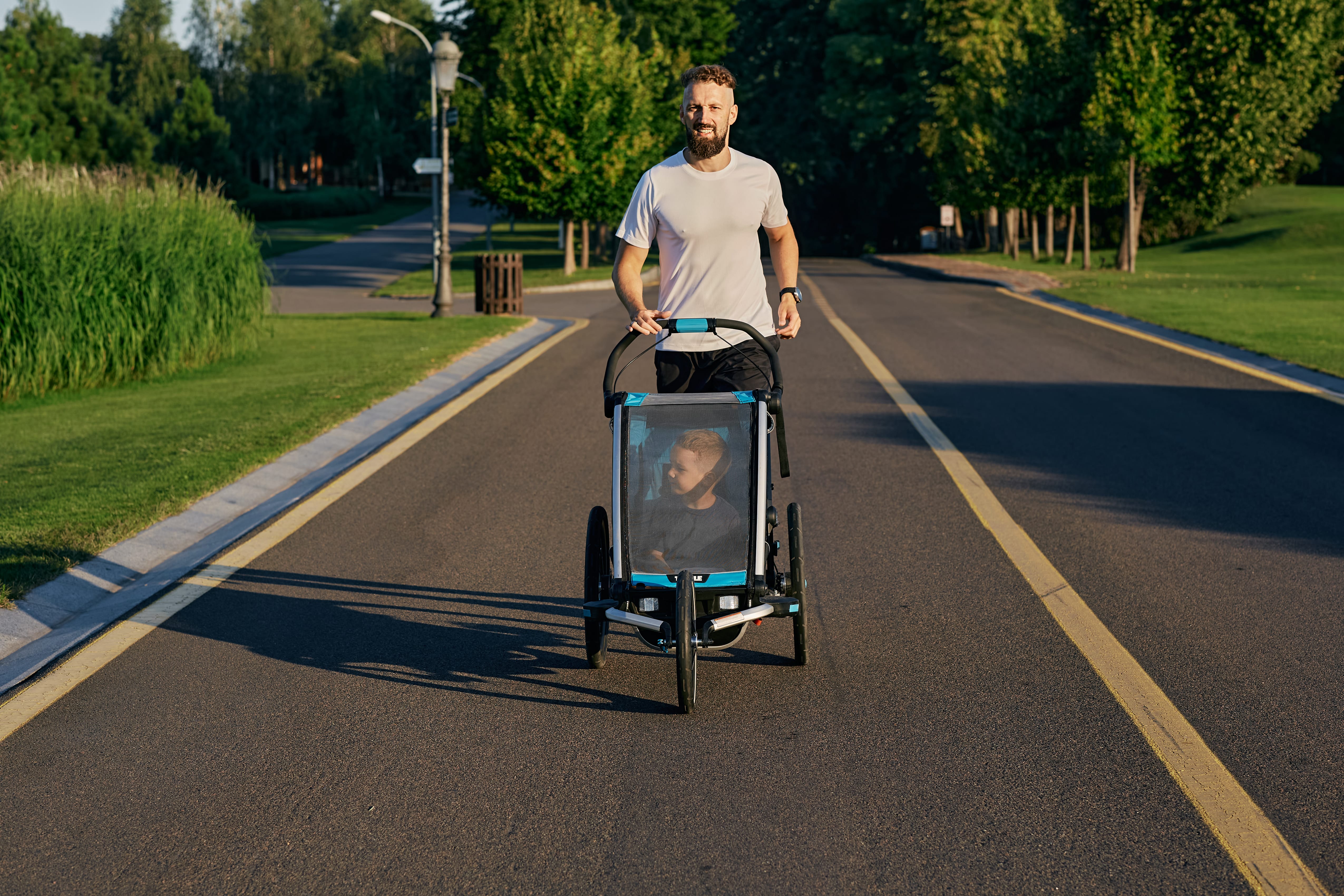 Young father with his kid in a running pram while jogging in a public park.