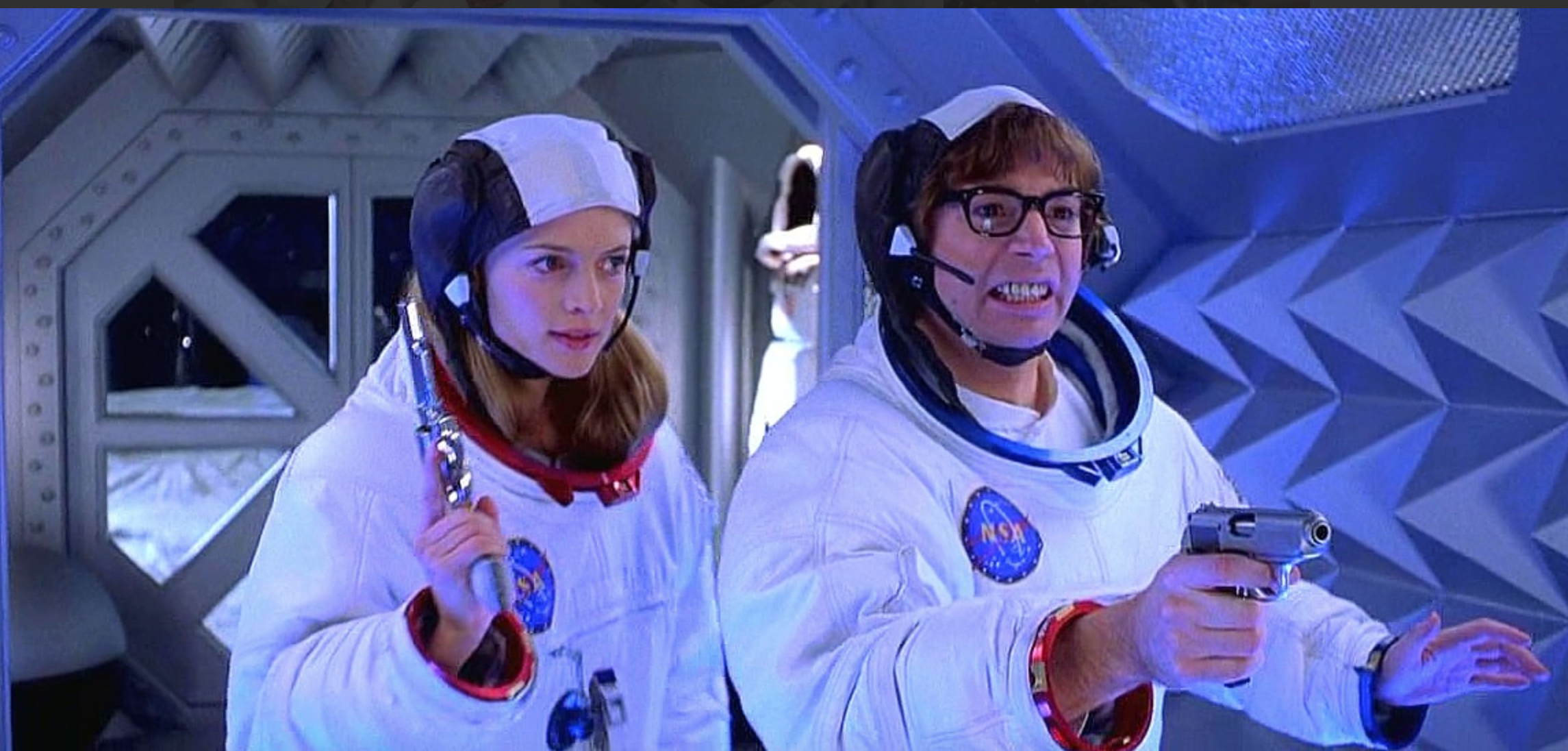A man and woman in a movie wearing Apollo spacesuits and holding handguns