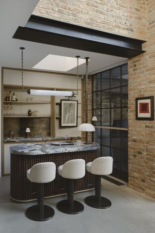 An indoor-outdoor home bar, with a marble counter, bar chairs, and a horizontal tube light