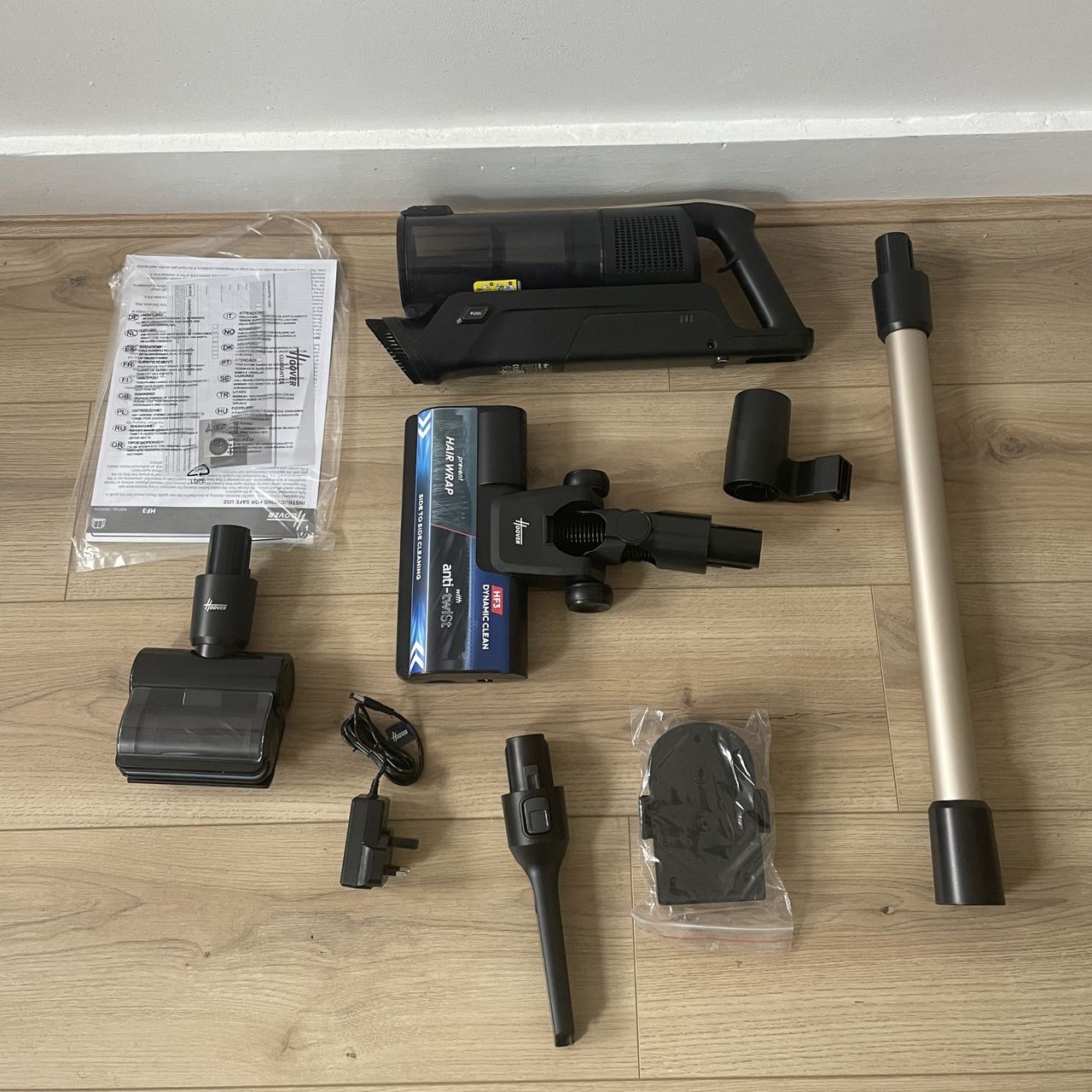 Components of the Hoover HF3 Pet DynamicClean Cordless Vacuum laid out on wood-effect flooring
