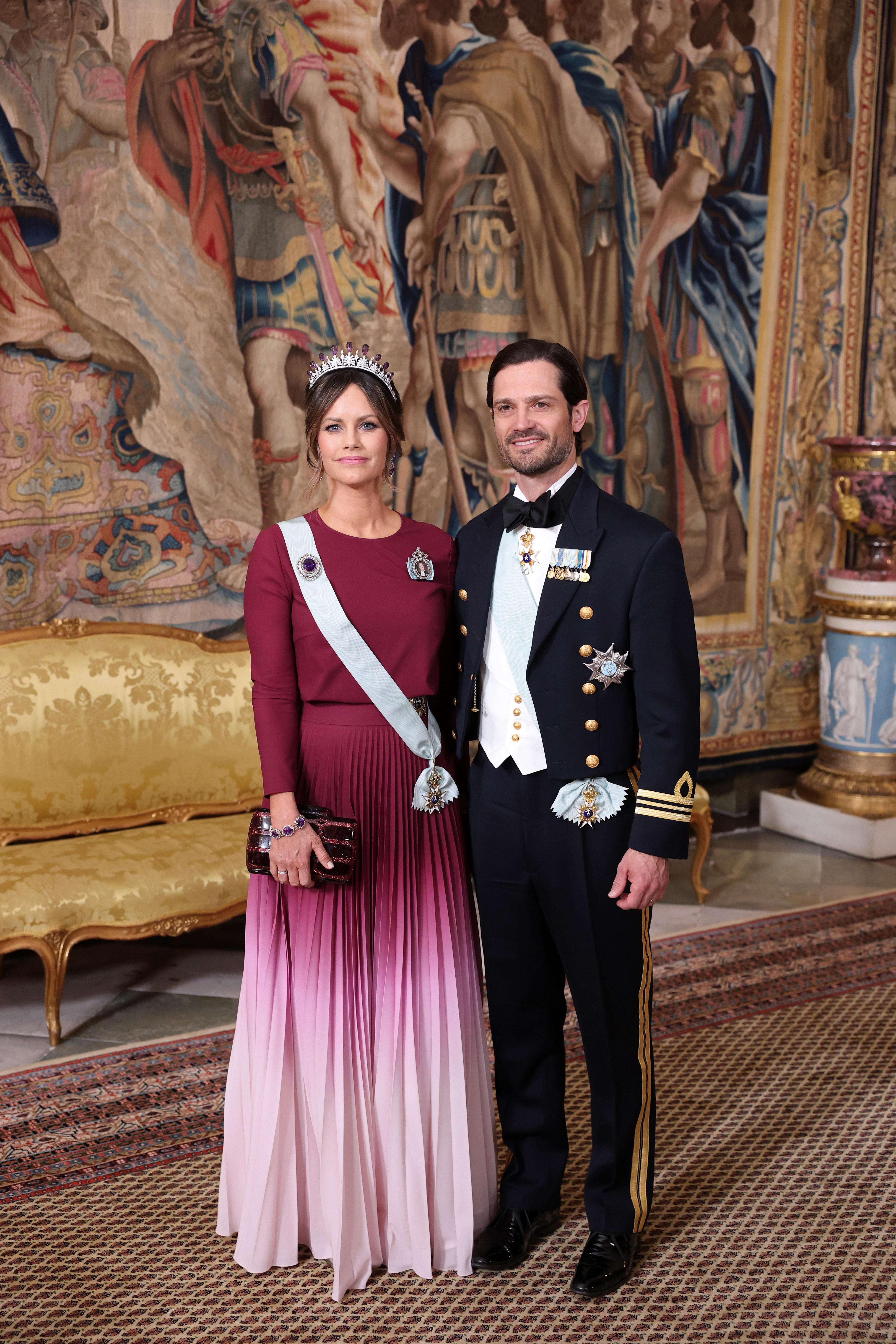 Princess Sofia and Prince Carl Philip in evening wear standing in front of a tapestry