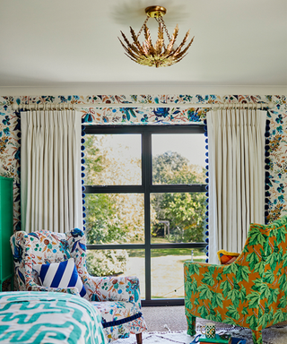 A bedroom with gold statement ceiling light hung above bed next to two patterned armchairs