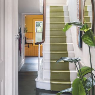 Hallway with green stair runner on painted white stairs.
