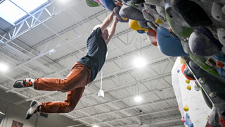 Linn Poston hanging from a handhold on a climbing wall