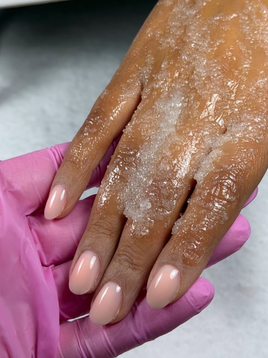 Hands with a hand scrub product being buffed into the hands, which are painted with a sheer peach milk colour