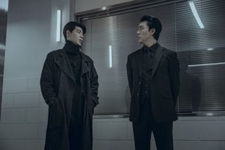 Bae Hyeon-seong as Seung-jo and Lee Mu-saeng as Kuroko 1, standing in an industrial building in front of a window with blinds, in Gyeongseong Creature S2.