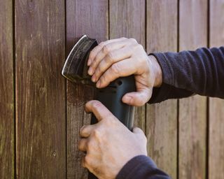 Man sanding a wooden fence with a electric sander