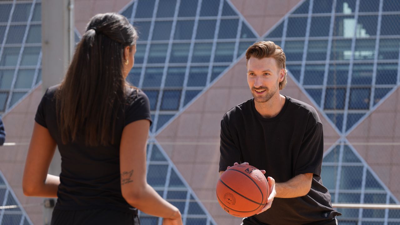 A man and a woman playing basketball, the man is holding the ball, while the woman's back is turned to the camera