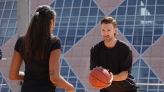 A man and a woman playing basketball, the man is holding the ball, while the woman's back is turned to the camera