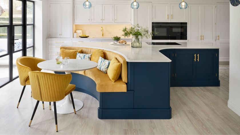 Curved blue kitchen island with built-in yellow seating and round table, set within a bright white kitchen with brass handles and pendant lights.