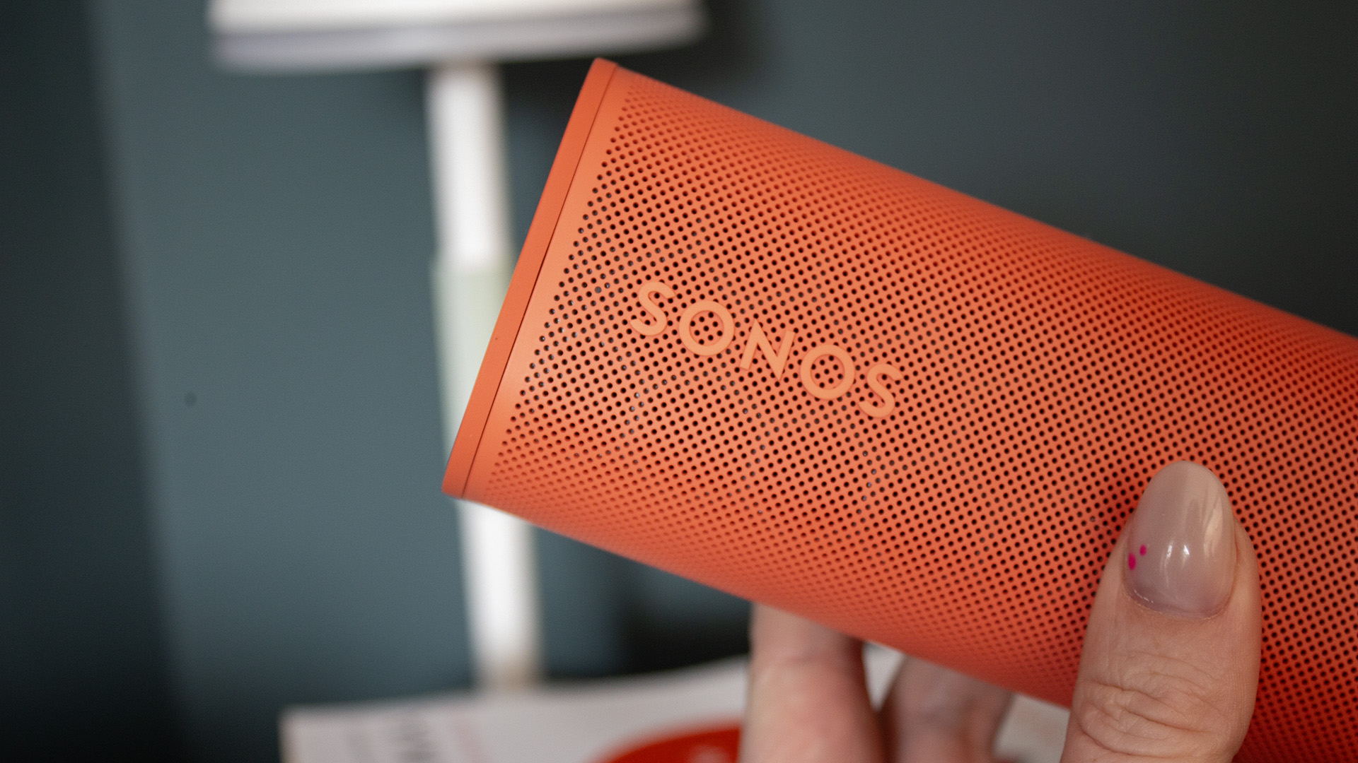 a red sonos roam 2 speaker in a living room on top of a red book