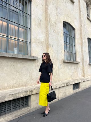 Eliza Huber wearing a black Carven sculpted top and yellow Prada satin skirt during Milan Fashion Week.