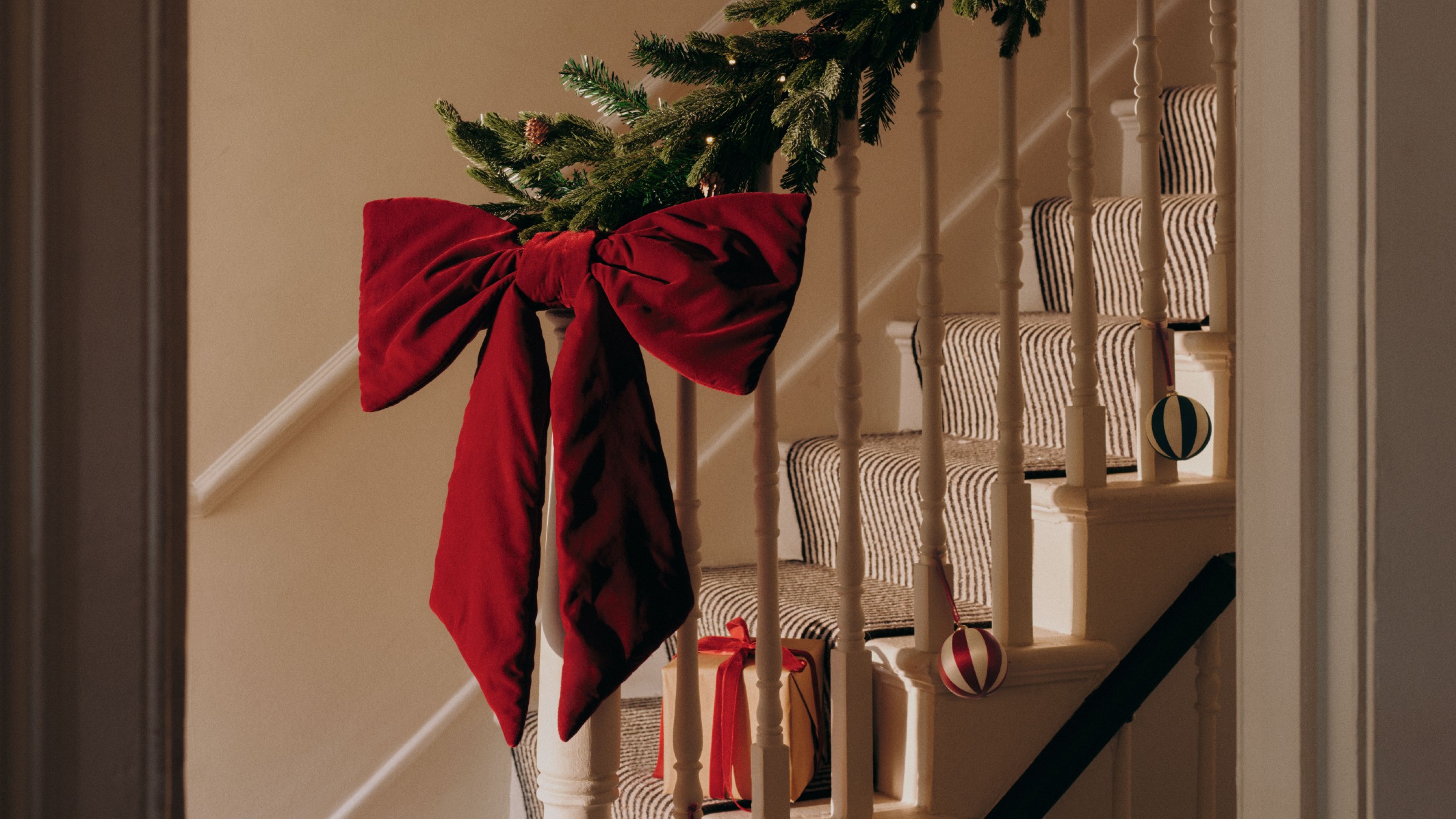 A staircase decorated with a Christmas garland and an extra large red velvet Christmas bow