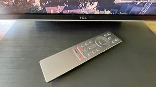 TCL 85C805K 4K TV remote on TV stand with bottom of screen and TCL logo
