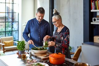A mature man and woman making a salad together in their kitchen.
