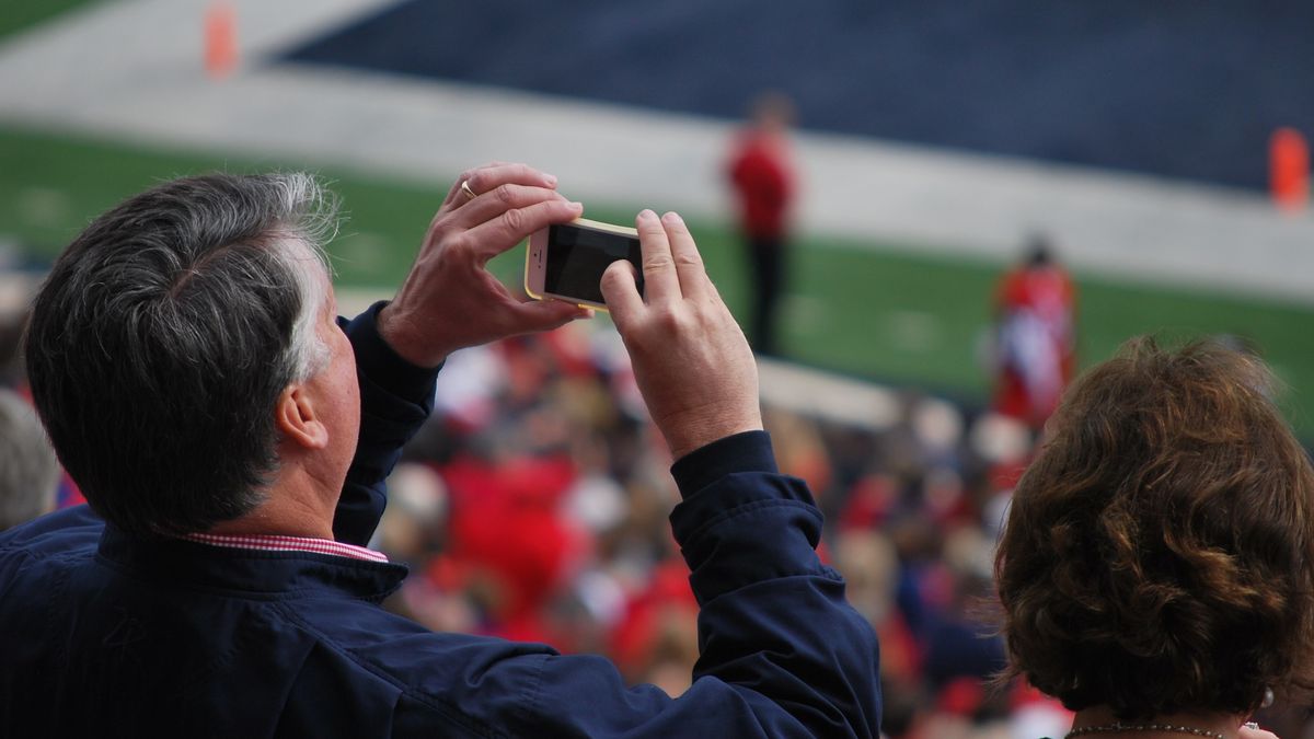 Man takes a picture on his smartphone at a stadium