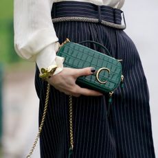 Woman wearing oud nails, one of the best winter nail colours for 2023, at Paris Fashion Week while holding a green Celine clutch bag