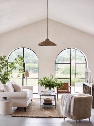 light and airy living room with textures, rattan pendant, sheepskin armchair, coir rug, wood, metal and glass coffee table, plants and greenery in vase