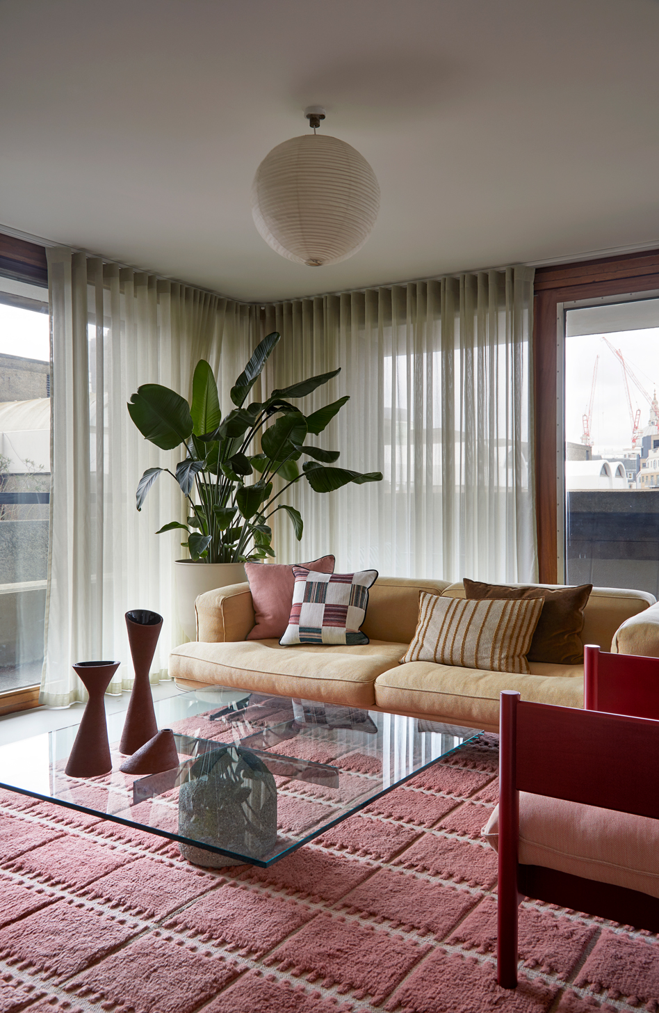 Image of a yellow sofa in a mid-century-feeling living room with a pink rug and windows on all of the walls.