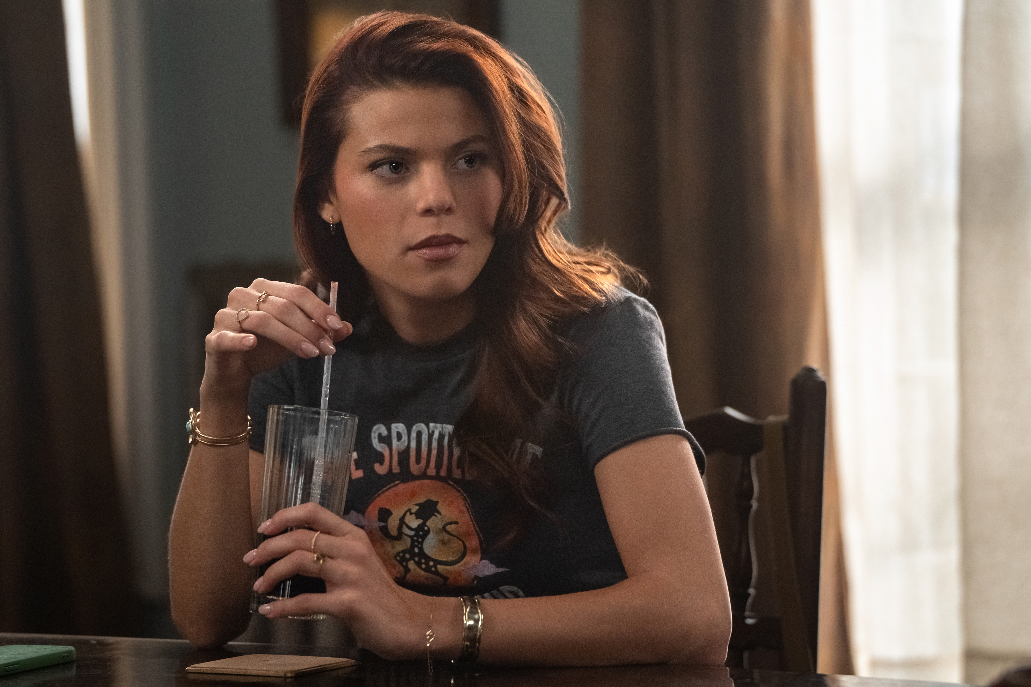 Heidi Grace Engerman as Sidney sits at a dining-room table while holding a glass with a straw, in Episode 205 of Netflix's 'Ransom Canyon' Season 2.