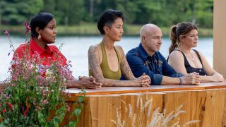 Michelle, Kristen, Tom and Gail sit at a wooden platform waiting to be served BBQ outside on Top Chef.
