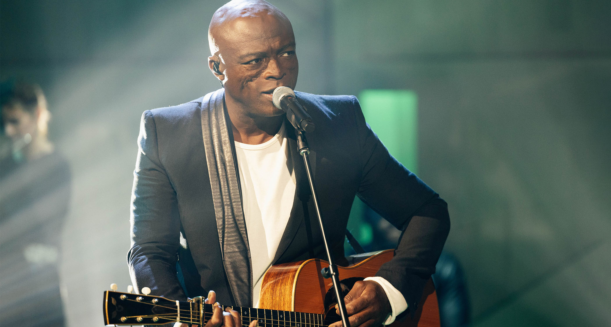 Seal performs live on NBC&#039;s The Kelly Clarkson Show wearing a dark suit jacket, white T-shirt, and playing an acoustic guitar capo&#039;d at the second fret.