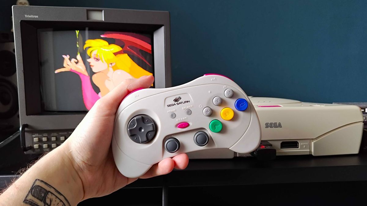 Hand holding Retro-Bit Sega Saturn Pro controller in front of matching white console and Sony PVM CRT TV with Vampire Hunter Darkstalkers Revenge cutscene on screen featuring Morrigan.