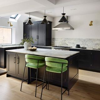 Kitchen with dark cabinetry, marble surfaces and green bar stools, with light wooden floorboards and 3 black pendant lights over the kitchen island