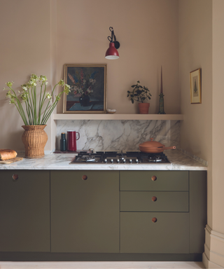 kitchen with dark green modern cabinetry and pale pink walls with grey marble surface top and rattan jug of flowers and red wall light
