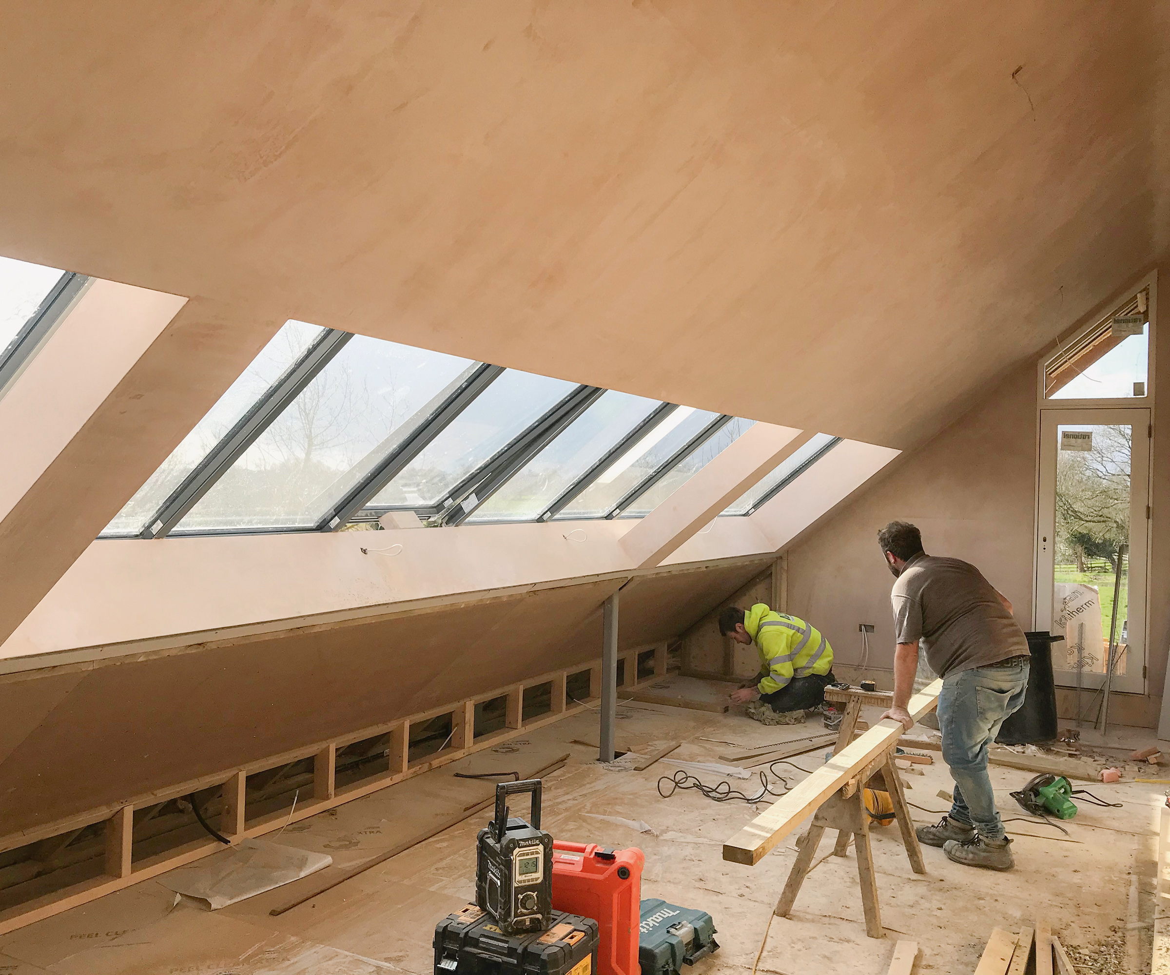 A loft room with a line of roof glazing with men working at fitting beams