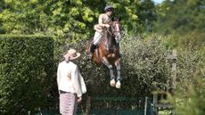 Rider demonstrating how to jump a bullfinch towards camera with working hunter judge in foreground