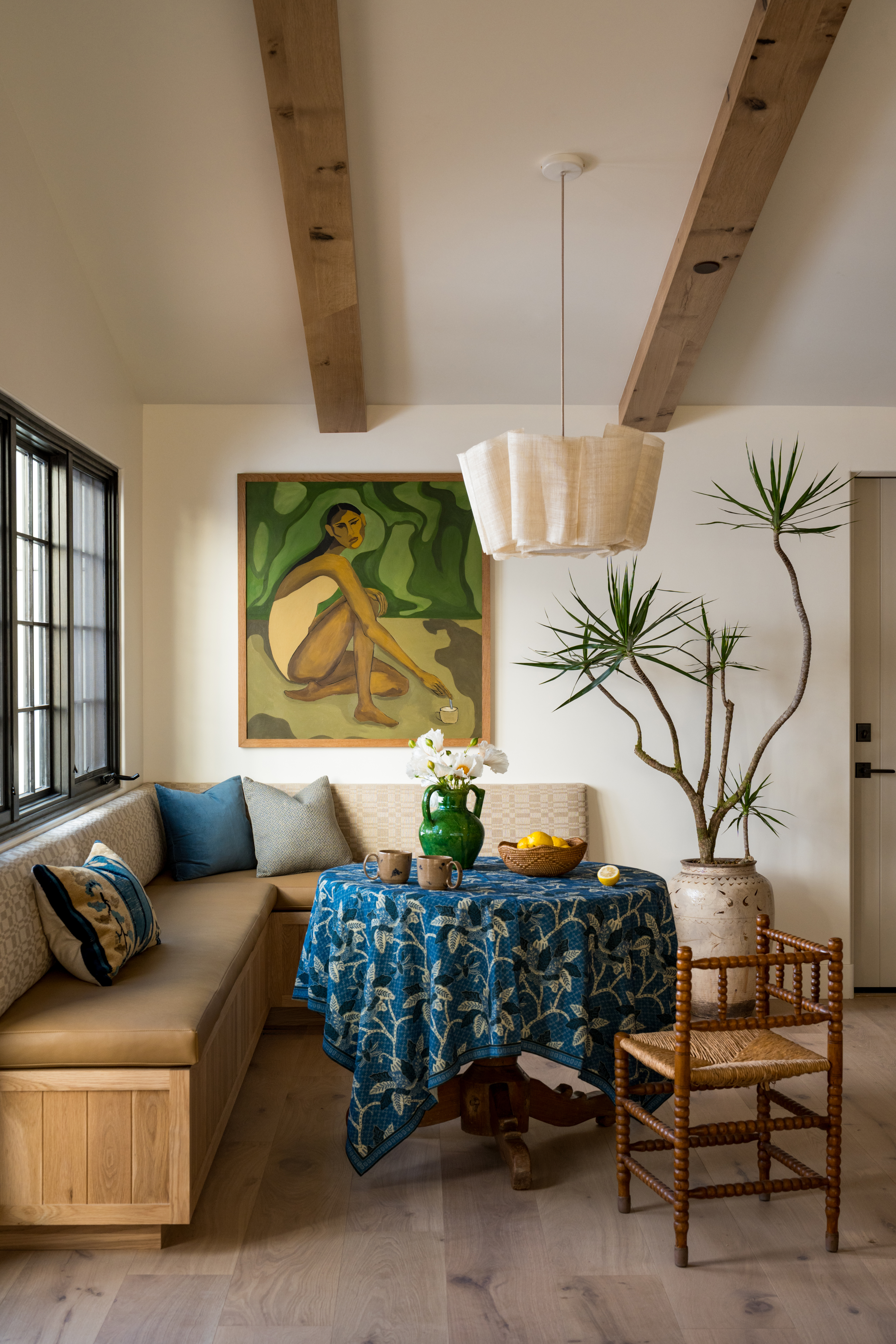 leather and fabric banquette in neutral tones with blue cushions and printed tablecloth, and a bobbin chair