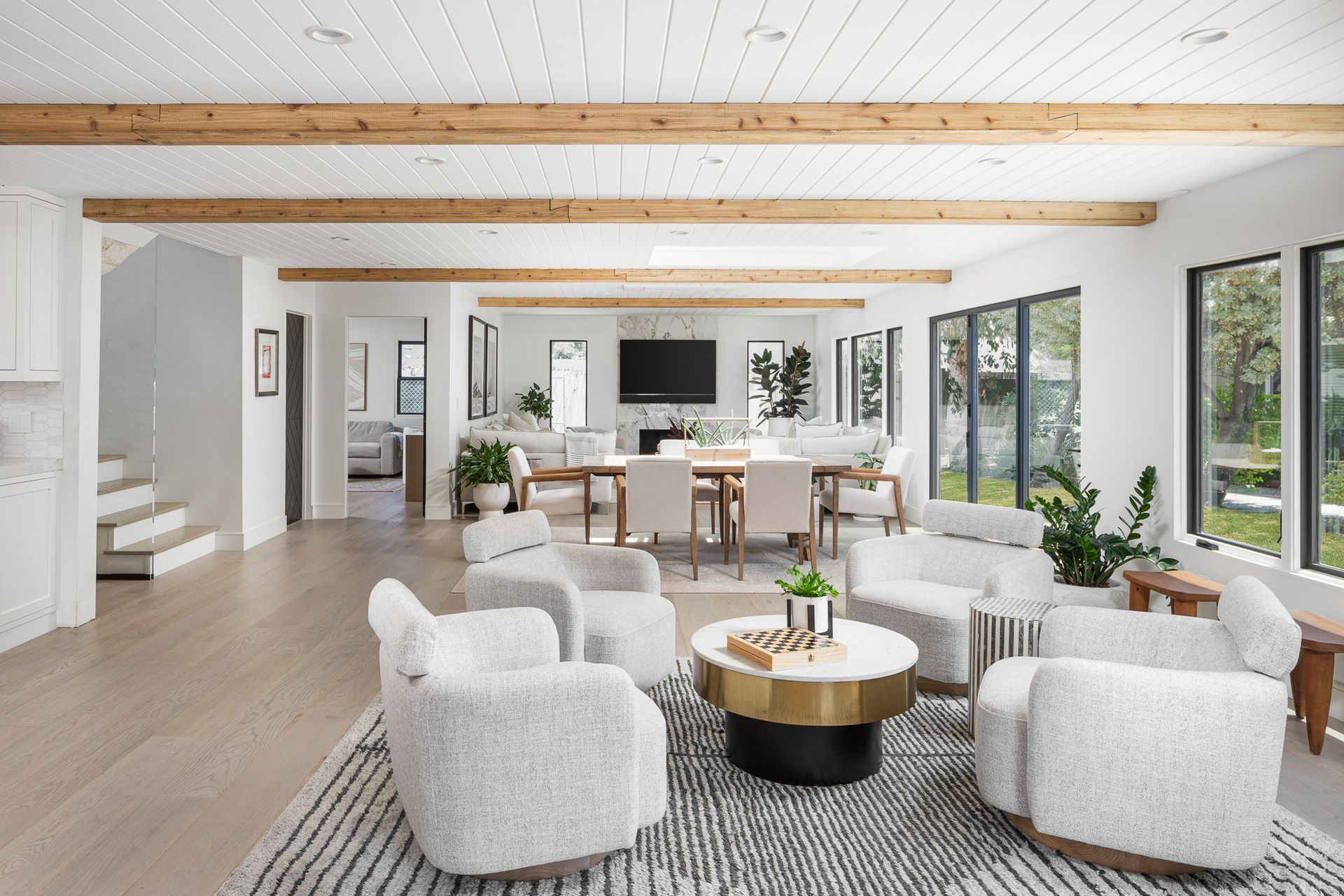 An open plan living room with a neutral palette, white armchairs around the coffee table, and a dining table in the background