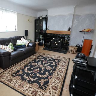 Small living room with a large rug and leather sofas, in need of renovation