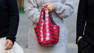 person holding red and gold stripe handbag