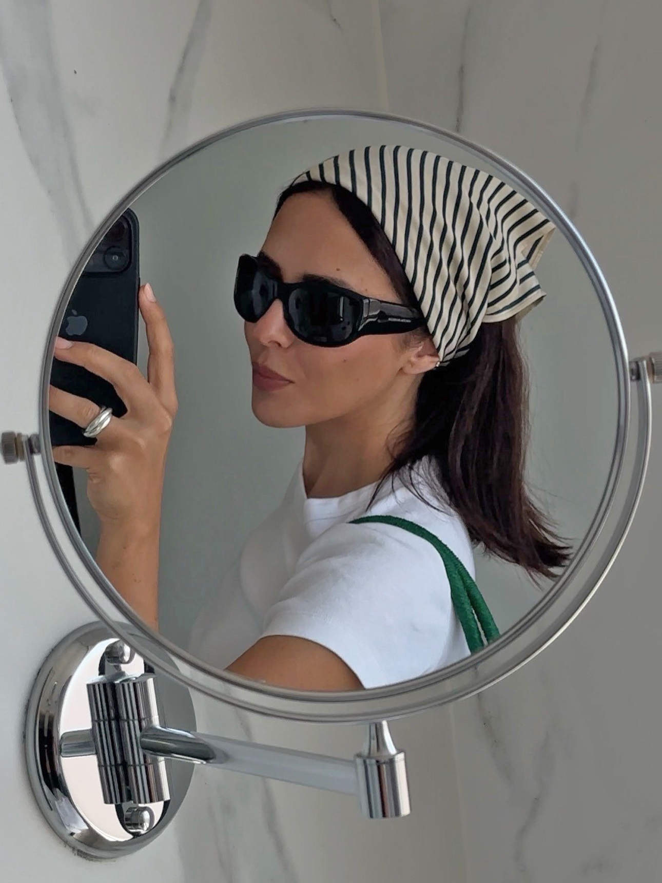 style influencer Debora Rosa poses for a mirror selfie wearing a striped head scarf, oversize sunglasses, a white T-shirt, and green shoulder bag