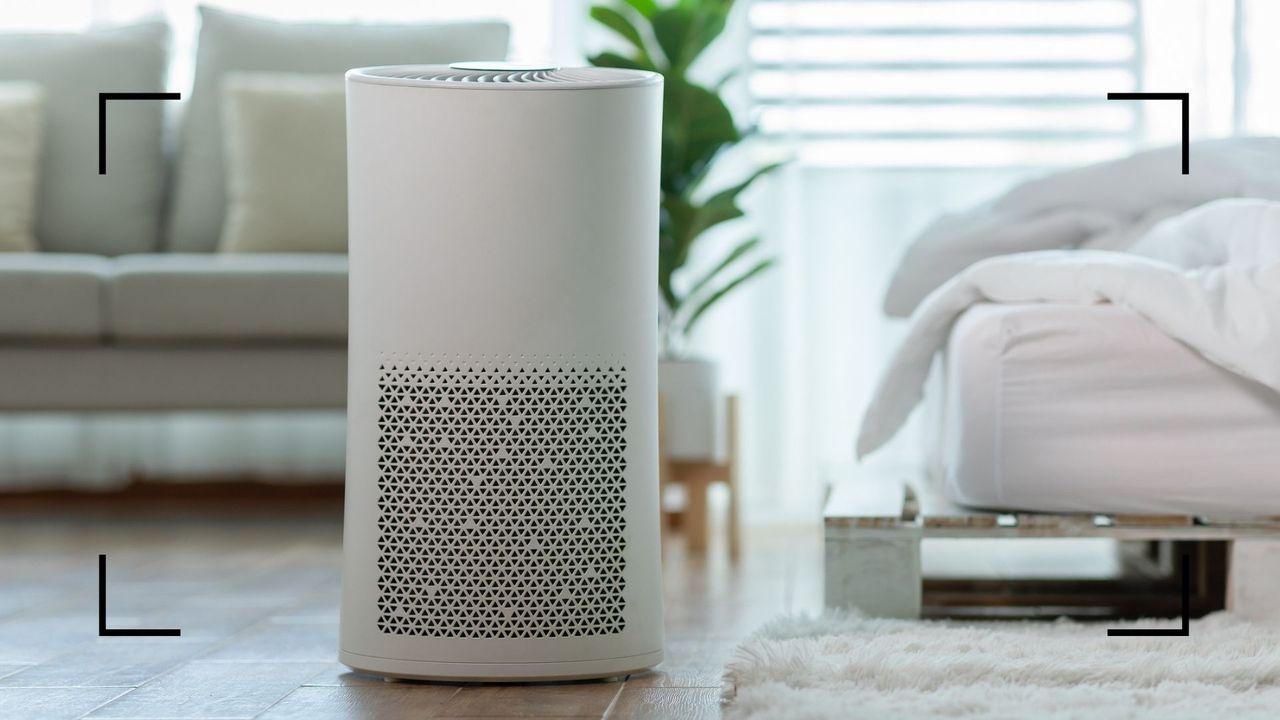 a white air purifier standing in a bedroom with the bed in the foreground