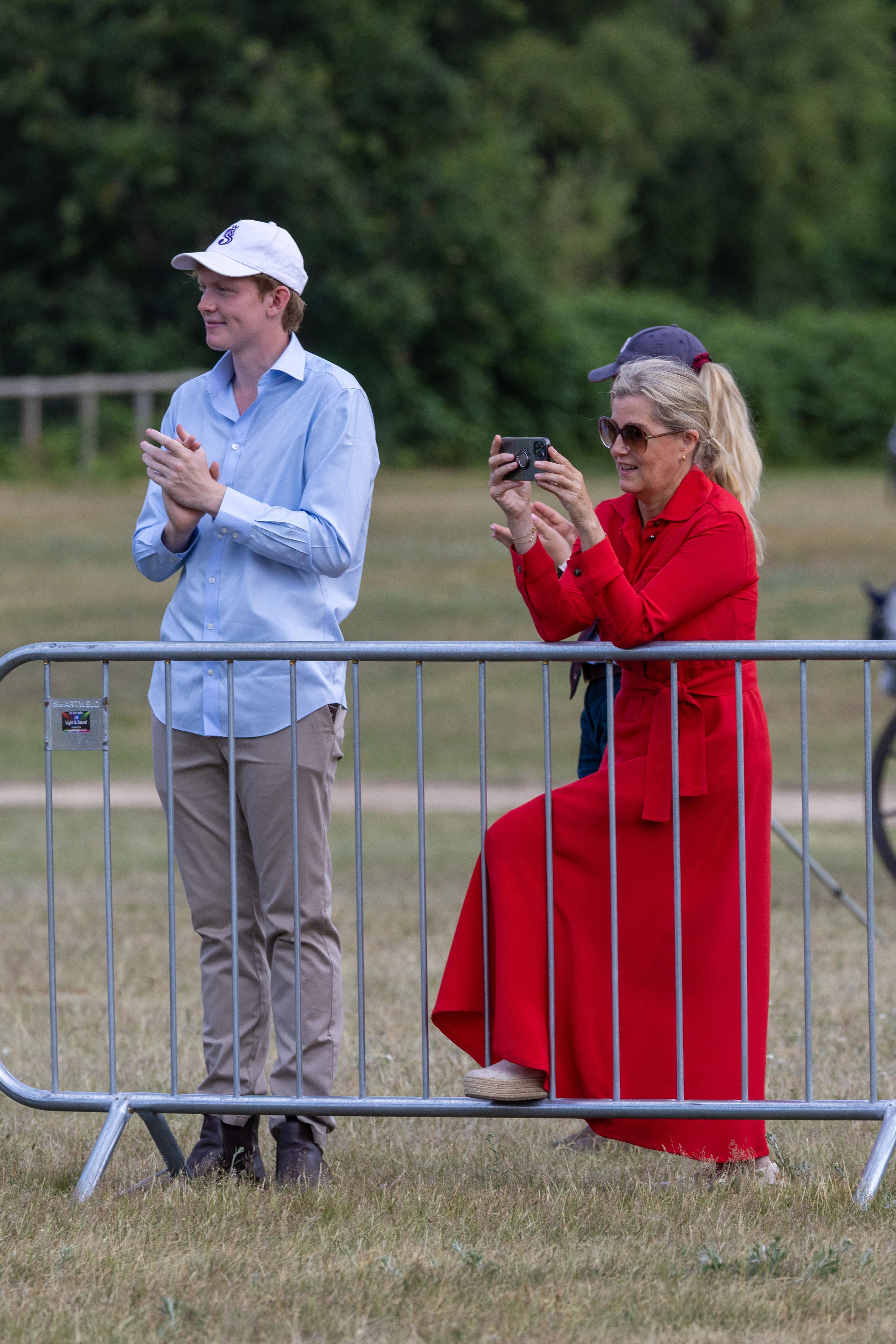Felix da Silva-Clamp clapping in front of a barrier next to Duchess Sophie, wearing a red dress and taking a photo