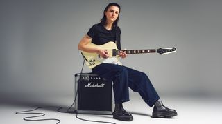Laura Cox holding an electric guitar and sitting on a Marshall amp