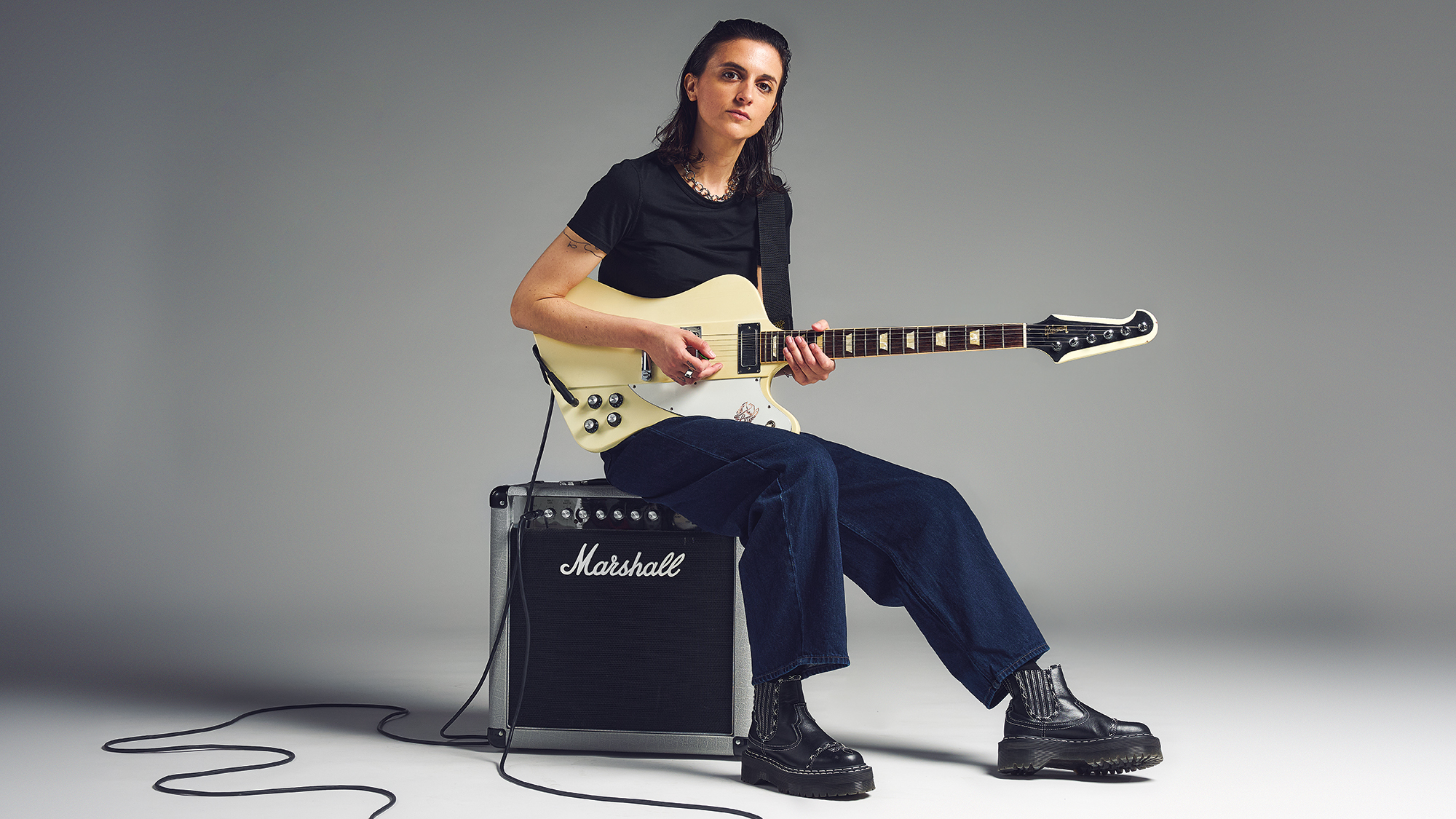 Laura Cox holding an electric guitar and sitting on a Marshall amp