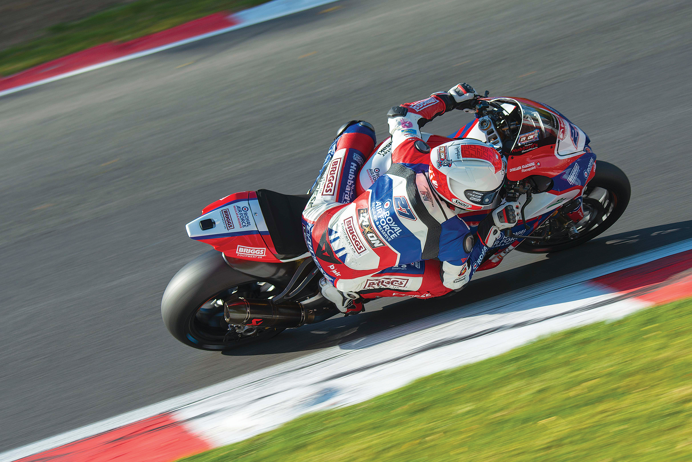 A racer in a blue and red suit leans into a curve on a motorcycle, showcasing speed and skill on a racetrack