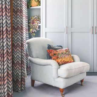 grey armchair in a bedroom with colourful curtains behind it, and grey wardrobes to its side