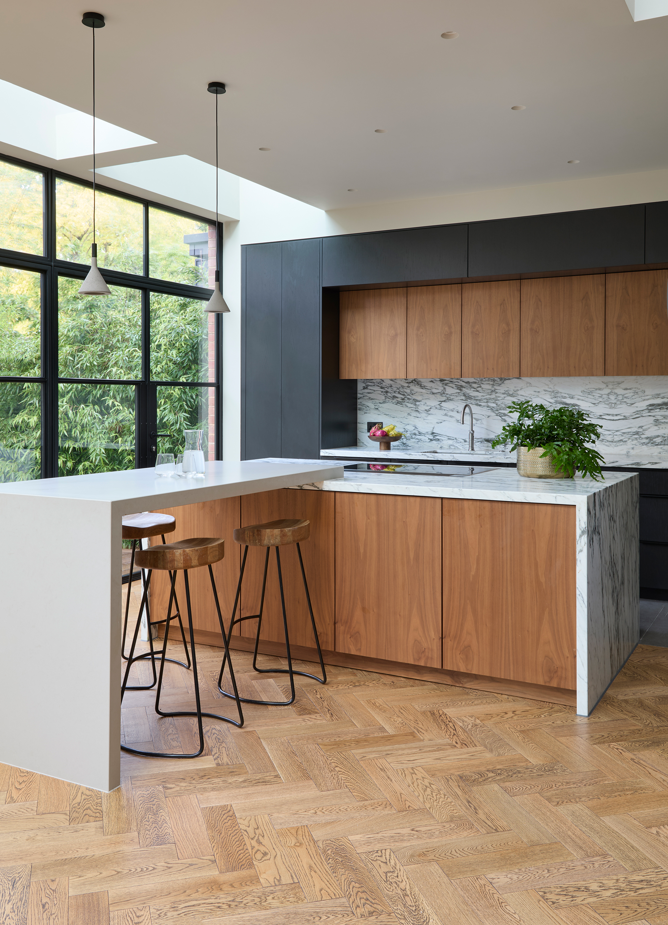A modern kitchen with a peninsula island, wooden herringbone flooring, and a marble countersplash